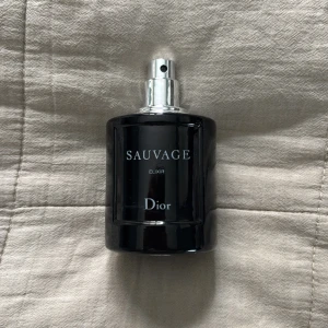 Dior Sauvage Elixir 90/100ml (inget lock)  - Dior Sauvage Elixir är en lyxig herrparfym i en mörkblå, nästan svart glasflaska med silverfärgad spraykork. Flaskan har en stilren, rund form och tydlig logga framtill. Doften är intensiv och maskulin, perfekt för dig som vill sticka ut.
