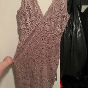 Ljuslila spetsklänning med v-ringning strl: 38 - Superfin ljuslila kortklänning med v-ringad hals och figurnära passform. Klänningen har ett vackert spetslager över ett slätt innerfoder och är ärmlös. Perfekt för dig som vill sticka ut med en elegant och romantisk look.