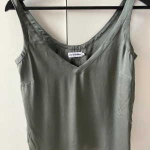 Grågrön linnetopp från Ahlvar Gallery - Säljer en stilren grågrön linnetopp från Ahlvar Gallery i storlek XS. Toppen har v-ringning och är ärmlös med en mjuk, glansig finish som ger en lyxig känsla. 93% silke nyköp 1500kr knappt använd, Perfekt att matcha med jeans eller kjol för en clean look.