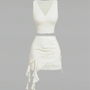 Vit spetsig croppad linnetopp som ch en kjol  - Säljer en vit croppad linnetopp med v-ringning och broderade spetsdetaljer. Toppen är ärmlös och har en figurnära passform. Perfekt för sommarens varma dagar och ger en romantisk vibe med sitt fina spetsmönster. Kjolen är väldigt cute och är perfekt för vår och sommar.