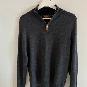 Mörkgrå Merinoulls Half Zip från  Morris - Snygg mörkgrå tröja från Morris i 100% merinoull. Tröjan har half zip med läderdetalj på dragkedjan och diskret broderad logga på. perfekt till jeans eller chinos. Inga defekter/skador då tröjan är helt ny!🙌