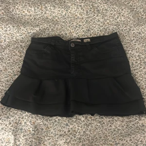 Svart volangkjol  - Snygg svart kortkjol jag sytt själv med volang nertill och kjolen är i skinn (ej äkta). Kjolen har både fram- och bakfickor samt knapp och dragkedja framtill. Perfekt för dig som gillar en trendig och cool stil. kommer ej till användning då den är för liten 