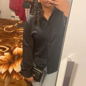 Svart skjorta från BikBok i storlek L - Stilren svart skjorta från BikBok i storlek L. Skjortan har klassisk krage, knäppning framtill och långa ärmar. Materialet känns mjukt och har en lätt glansig finish som ger en snygg look. Perfekt att styla med jeans eller kjol.