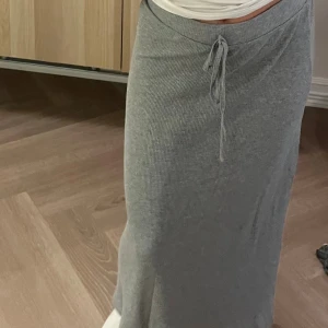 Grå ribbad långkjol med snörning - Säljer en grå långkjol med ribbad struktur och snörning i midjan. Kjolen har en enkel och stilren design som är lätt att matcha med olika toppar. 