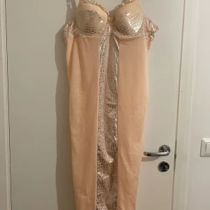 En biege nättlinne storlek M -  En biege nättlinne  med glansiga detaljer och leopardmönster upptill och längs mitten. Klänningen har smala axelband, vadderad byst och en snygg krokknäppning i ryggen. Materialet känns mjukt och lätt, perfekt för dig som vill sticka ut.