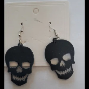  Helt nya Svarta döskalleörhängen - Helt nya  örhängen i form av svarta döskallar med urklippta ögon och mun. Perfekta för dig som gillar edgy accessoarer och vill sticka ut. Hängande modell med metallkrok. Säljs som par.