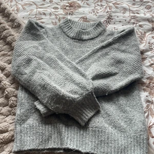 Grå stickad tröja - Mysig grå stickad tröja med ribbade muddar.Tröjan har lång ärm och en klassisk, enkel design som passar perfekt till kyliga dagar. Materialet är mjukt och ger en avslappnad men ändå stilren look.