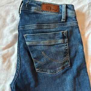 Blå jeans från LTB med raka ben - Snygga blå jeans från LTB med klassisk femficksdesign och raka ben. Jeansen har en mellanblå tvätt, kontrastsömmar och läderpatch med logga bak i midjan. Perfekta för en avslappnad och stilren look.