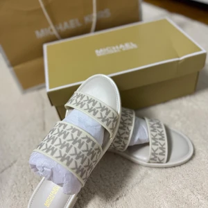 Michael Kors Kennedy Jelly sandaler - Snygga sandaler från Michael Kors i modellen Kennedy Jelly Slide. Skorna är i en ljus vaniljvit färg med två breda remmar i textil med MK-logga i mönster. Sula i syntetmaterial med präglad MK-detalj undertill. Perfekta för sommaren och riktigt trendiga.