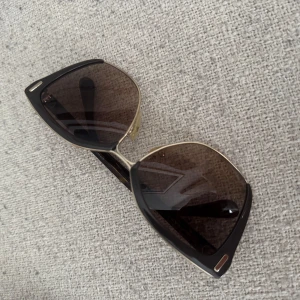 Prada solglasögon - Solglasögon från Prada med  cat-eye form och svarta bågar i kombination med guldfärgade detaljer. Glasen är mörka och har en lätt toning. Kommer med originalfodral från Prada. 