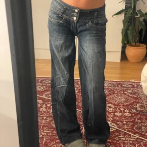 Mörkblå wide jeans med låg midja - Säljer ett par mörkblå jeans med snygg tvätt, låg midja och tre knappar framtill. Modellen är loose och wide med raka ben och coola detaljer på fickorna. Ps: hål mellan benen men går att fixa och syns inte när man går/står! De är även lite insydda i midjan men går att spreta upp! Sitter bra på min midja som är w27 och kan tänka mig att det passar fler storlekar! Enkla jeans att jobba med :)