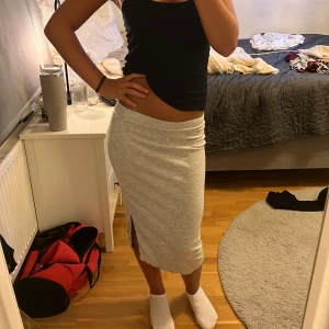 Ljusgrå ribbad långkjol från H&M - Säljer en ljusgrå ribbad långkjol från H&M. Kjolen är figurnära med en liten slits på sidan och har en mjuk, stretchig känsla. Perfekt för dig som gillar enkel och stilren look. Passar dig som vill ha en bekväm men snygg kjol till vardags.