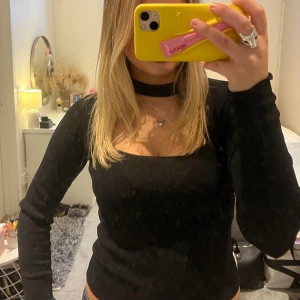 Svart festtopp - Säljer en svart långärmad topp med fyrkantig urringning och inbyggd choker-detalj vid halsen. Snygg och stilren modell som sitter tight och framhäver figuren. Perfekt för dig som gillar trendiga och unika detaljer.