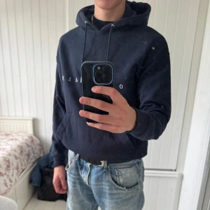 Mörkblå hoodie från Jack & Jones - Mörkblå hoodie från Jack & Jones Originals med vit text på bröstet. Klassisk känguruficka, snörning i huvan och mjukt material. Perfekt för chill dagar och enkel att matcha med jeans eller joggers. Hör av dig vid frågor!