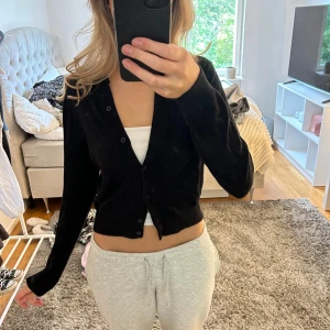 Svart kofta med knappar - En svart, klassisk kofta med knappar framtill. Modellen är croppad och har lång ärm. Perfekt att slänga över ett linne eller t-shirt för en chill och stilren look. Enkel och tidlös design som passar till det mesta.