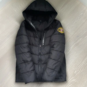 Svart pufferjacka från Zavetti Canada. Helt ny!!! - Svart pufferjacka från Zavetti Canada med huva och broderad logga på ärmen. Jackan har quiltad design, dragkedja framtill och en riktigt skön, vadderad känsla. Perfekt för kalla dagar och har en clean, modern look.