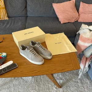 Axel Arigato - Snygga gråa sneakers från Axel Arigato i mjuk mocka med vit platt sula och rund tå. Klassisk låg modell med snörning och stilren design, perfekt för dig som gillar minimalistiska och cleana skor. Kommer med originalkartong. Använda 5-6 gånger 