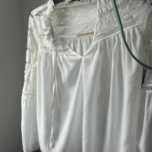 Vit spetsblus från Boohoo - Supersöt vit blus från Boohoo med spetsdetaljer upptill och på ärmarna. Blusen har v-ringning med knytband och långa ärmar. Perfekt för dig som gillar romantisk och bohemisk stil.