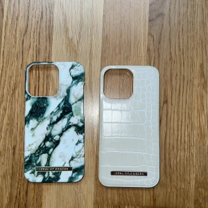 iDeal of Sweden skal till iPhone 13 pro  - Två snygga iDeal of Sweden-skal för iPhone, ett med marmormönster och ett med vit krokodilstruktur. Båda i mycket fint skick utan synligt slitage. Ger bra skydd och stil till din iPhone. Passar modeller med stor kameralins, t.ex. iPhone 13 pro. Kan köpas 2 för 150 kr annars 1 för 100 kr. Använd ändas fåtal gånger