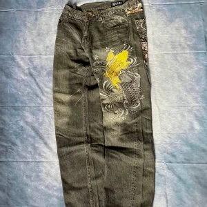 Japan Blue Y2K 2000s Jeans – Yellow Koi Fish Embroidery - Rare Japanese Y2K 2000s era denim by Japan Blue, featuring bold yellow koi fish embroidery on the front leg and traditional floral jacquard/embroidered details across three pockets. Iconic early 2000s Japanese streetwear piece with a unique wash and detailed stitching.  W34/L33  📏 Measurements (cm): Waist: 41.5  Hips: 45 Back rise: 30 Thigh: 32.5 Knee: 24.5 Leg opening: 22.5 Inseam: 84  Outseam: 109  ✅ Condition: 100% wearable. There was a repair ask for it pictures