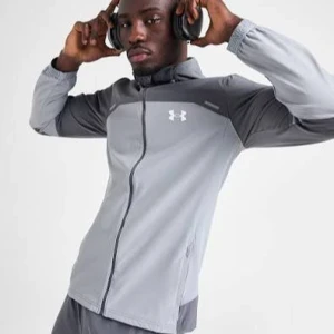 Grå vindjacka från Under Armour - Snygg grå vindjacka från Under Armour med huva och dragkedja framtill. Jackan har två olika grå nyanser, elastiska muddar och logga på bröstet samt stor text på ryggen. Perfekt för träning utomhus och sportiga outfits. Även perfekt present för sig själv eller pojkvän