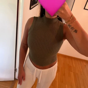 Olivgrön ribbad ärmlös polotopp - Säljer en olivgrön, ribbstickad polotopp med hög hals och croppad passform. Toppen är ärmlös och har en tight passform🩷