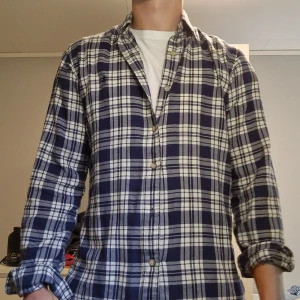 Rutig skjorta från Polo Ralph Lauren - Säljer en klassisk rutig skjorta från Polo Ralph Lauren i blått och vitt. Skjortan har lång ärm, knappar framtill och en liten broderad logga på bröstet. Modellen är custom fit och passar perfekt till en avslappnad stil.