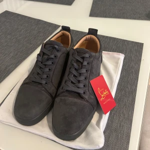 Christian Louboutin svarta sneakers mocka - Snygga svarta sneakers från Christian Louboutin i lyxig mocka med klassiska röda sulor. Skorna har rund tå, svarta snören och diskreta detaljer. Insidan är fodrad i beige skinn för extra komfort. Perfekta för dig som vill sticka ut med exklusiv stil. Använda i lite under en vecka, alltså i extremt bra skick. Storlek 43 men passar nog både 42 och 44