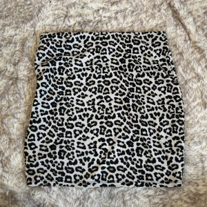 Leopardmönstrad kortkjol från Amisu - Snygg kortkjol från Amisu med leopardmönster i svart och beige. Kjolen har en rak passform och är tillverkad i ett mjukt, stretchigt material. Resår i midjan.