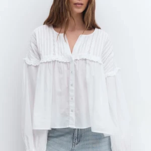 Vit blus med volang och knappar - Luftig vit blus med v-ringning, knappar framtill och volangdetaljer över bröstet. Långa ärmar med lätt puff och diskreta spetsinslag ger en romantisk vibe. Perfekt till jeans för en chill men ändå söt look.