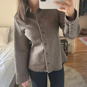 Brun firgursydd jeansskjorta zara - Snygg brun jeans skjorta med smockad midja och brun/khaki färg. 