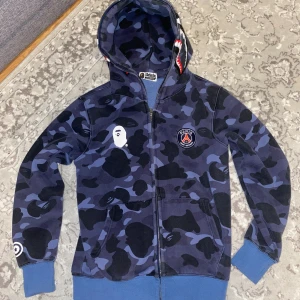 BAPE x PSG blå camo hoodie - Säljer en blå camo hoodie från BAPE x PSG. Sällan använd. Storlek XS. Snygg på både tjejer och killar. 