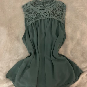 Grön ärmlös topp från ONLY - Supersöt grön topp från ONLY med vackert virkad spets upptill och knappar i nacken. Toppen är ärmlös, har en lös passform och faller snyggt. Perfekt för dig som gillar romantiska detaljer och en luftig känsla.