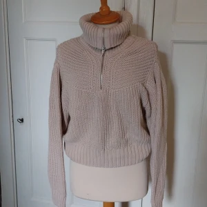 Beige stickad polotröja med half zip - Mysig beige stickad polotröja med grov struktur och ribbade muddar. Tröjan har en hög krage med half zip-dragkedja som kan bäras både uppvikt och nedvikt. Perfekt för lager-på-lager under kyliga dagar.