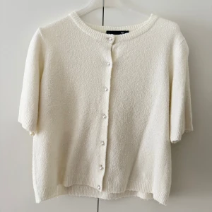 Vit kofta med kort ärm från lager 157 - Superfin vit kofta från lager 157 med korta ärmar och rund halsringning. Koftan är stickad i mjukt material och har knappar framtill. Perfekt att slänga över en topp för en chill och stilren look.