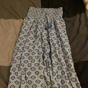 Blåmönstrad långkjol från Gina Tricot - Superskön långkjol från Gina Tricot i ljusblått och mörkblått med snyggt grafiskt mönster. Kjolen har smock i midjan och dekorativa knytband med tofsar framtill. Perfekt för dig som gillar flowy vibes och coola prints.