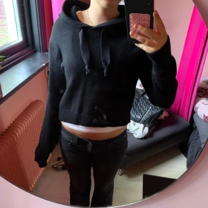 Svart croppad hoodie med huva - Svart croppad hoodie med huva och snörning i halsen. Tröjan har långa ärmar och ribbad nederkant. Perfekt för dig som gillar en avslappnad och trendig stil.