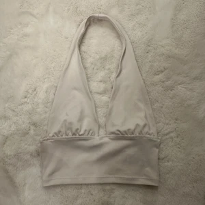 Vit halterneck topp från H&M Divided - Säljer en stilren vit halterneck topp från H&M Divided i storlek XS. Toppen är ärmlös med djup urringning och bred resår under bysten. Perfekt för dig som gillar minimalistisk och trendig stil. Materialet är mjukt och stretchigt, vilket gör den bekväm att bära.