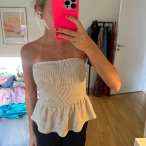 Beige stickad bandeau tubtopp - Superfin beige stickad bandeau tubtopp med volangkant nedtill. Vet ej märke, storlek Xs