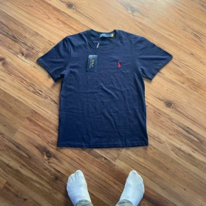 Marinblå t-shirt från Polo Ralph Lauren - Marinblå t-shirt från Polo Ralph Lauren i mjuk bomull 😎                                                                   - Size S/170                                                                 - Längd (64 cm) bredd (47 cm) ärm (20 cm)  - 10/10 skick, aldrig använd, kommer med tag   Hör av er gärna 👌