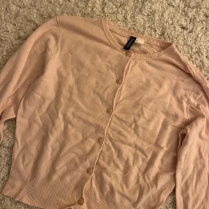 Ljusrosa kofta från H&M Divided - Söt ljusrosa kofta från H&M Divided i storlek S. Koftan har rund halsringning, långa ärmar och knäppning framtill med matchande knappar. Tillverkad i mjuk bomullsmix, perfekt att slänga över en topp eller klänning.