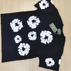 Svart t-shirt från Denim Tears L - Svart t-shirt från Denim Tears i storlek L med stora vita blommiga tryck över hela tröjan. Klassisk passform med rund hals och korta ärmar. Tillverkad i Portugal, riktigt snygg och unik design som sticker ut.