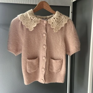 Beige kofta med spetskrage & Other Stories - Supersöt beige kofta från & Other Stories med korta ärmar, två fickor framtill och stora klädda knappar. Koftan har en unik, bred spetskrage i ljusbeige. Stickad i mjukt material. Använd 3 gånger! TRYCK INTE PÅ KÖP NU! Kontakta mig först💗💗