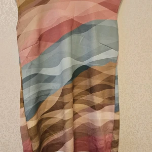 Ärmlös klänning med vågigt mönster - Säljer en ärmlös klänning med unikt vågigt mönster i toner av rosa, blått, beige och brunt. Klänningen har en rak passform och är tillverkad i ett slätt, lätt material som ger ett snyggt fall. Perfekt för dig som gillar färg och grafiska mönster.