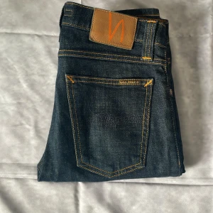 Nudie Jeans 29/32 - Snygga mörkblå jeans från Nudie med klassisk femficksdesign och kontrastsömmar i orange. Nypris 1600kr, mitt pris 499kr. Skick 9,5/10, inga defekter, som nya!