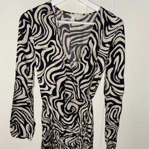 Zebramönstrad omlottklänning - Snygg kort omlottklänning från H&M med svartvitt zebramönster. Klänningen har långa ärmar, v-ringning och omlott i midjan