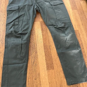 Mörkgröna cargopants med raka ben - Snygga mörkgröna cargopants med raka ben och stora fickor på sidorna. Byxorna har klassisk cargostil med bälteshällor och är tillverkade i ett slitstarkt bomullstyg. Perfekta för en avslappnad och trendig look.