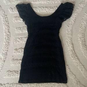 Svart spetsklänning med volangärm - Supersnygg svart kort klänning med spets och volangärmar från h&m. Figurnära passform och rundad halsringning.