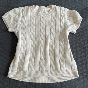 Ljusrosa kabelstickad tröja Gina Tricot - Söt kabelstickad tröja från Gina Tricot i ljust rosa. Tröjan har korta ärmar, rund halsringning och breda ribbade muddar. Perfekt för lager-på-lager och ger en chill men ändå stilren vibe.