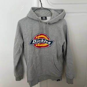 Grå Dickies hoodie med logga - Säljer en grå hoodie från Dickies. Tröjan har huva med snörning, magficka och ribbade muddar. Perfekt för dig som gillar streetwear och vill ha en chill look.